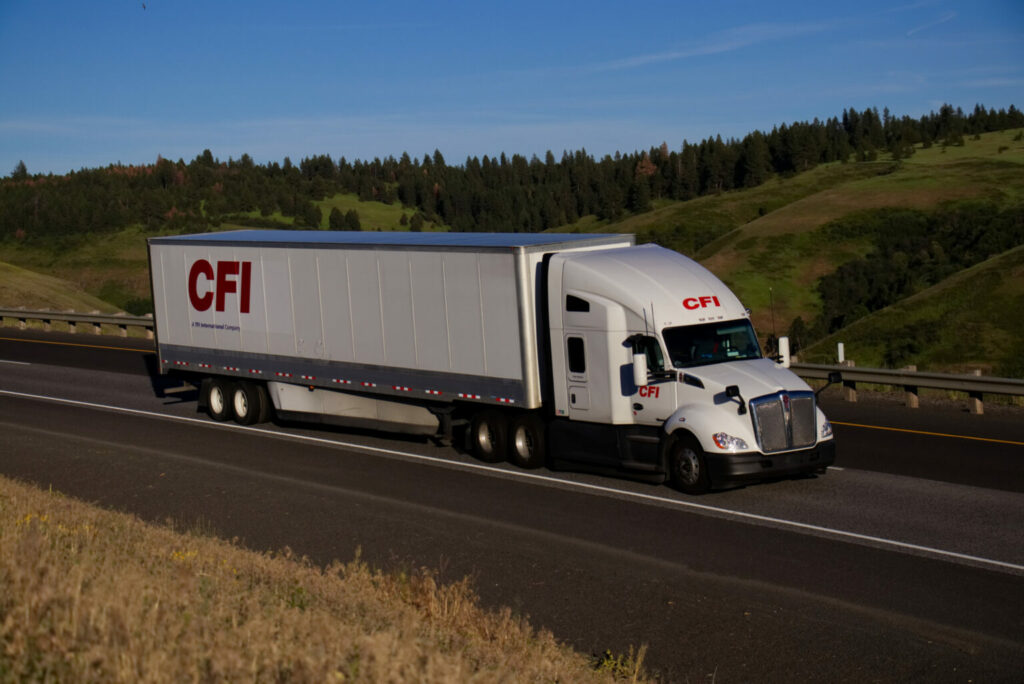 Camion et remorque CFI blancs sur route avec arrière-plan verdoyant.