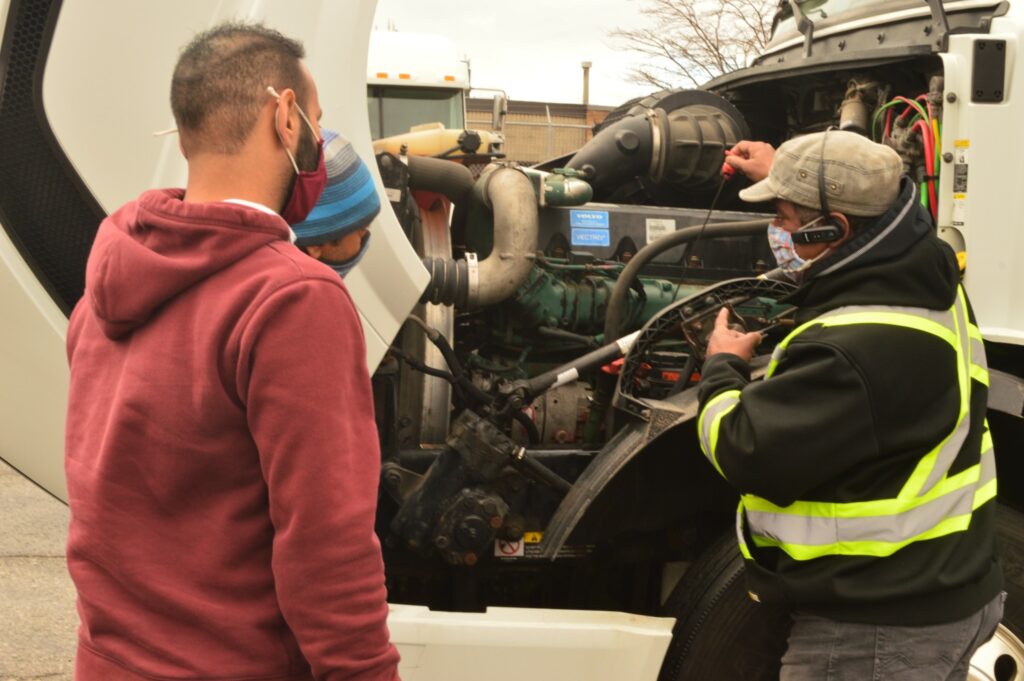 Formateur et deux recrues autour du capot ouvert d’un camion.