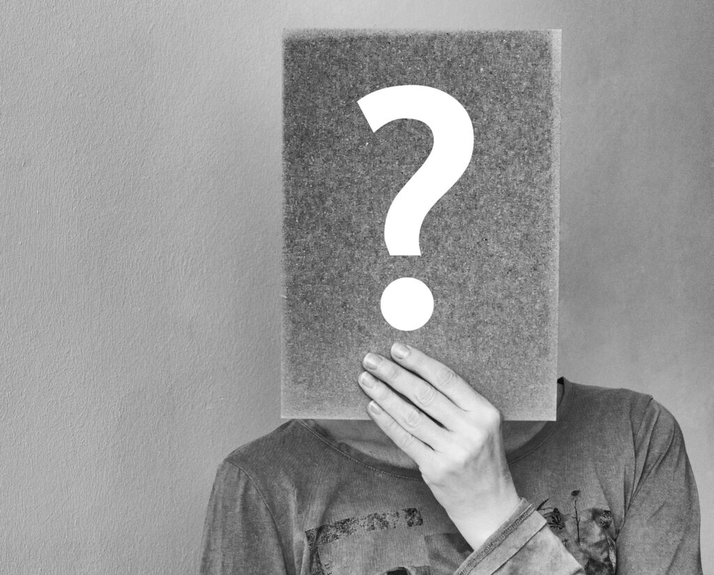 Portrait noir et blanc d’un homme dont le visage est caché par un panneau où apparaît un point d’interrogation.
