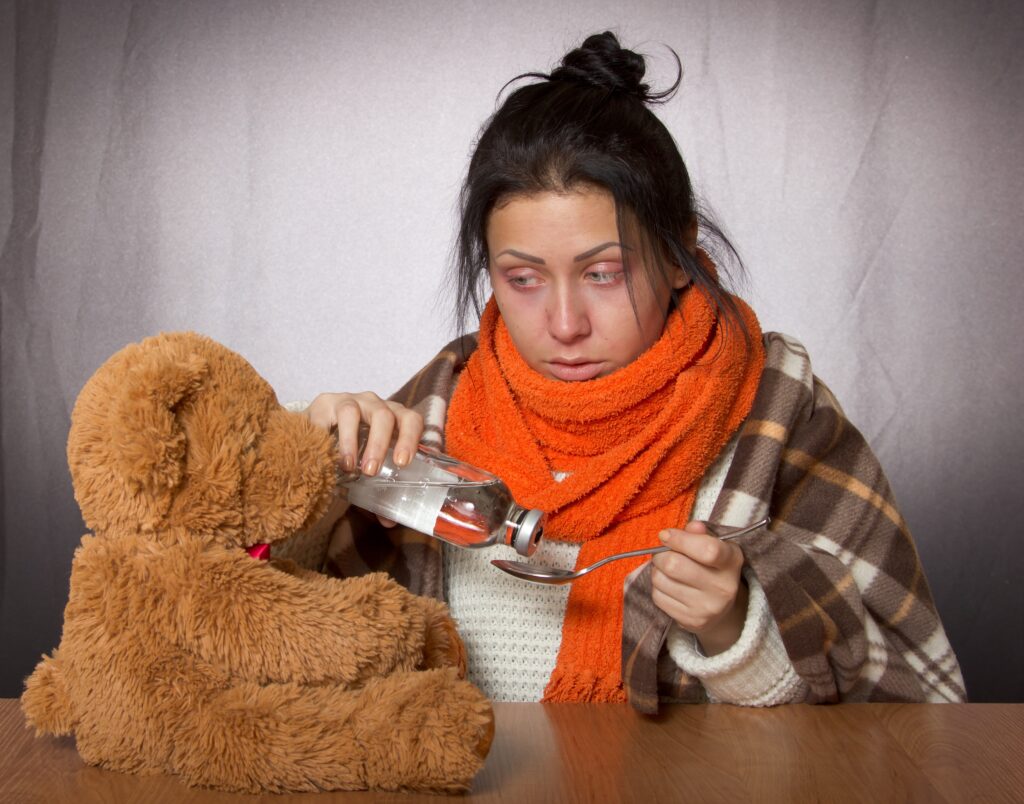 Jeune femme enrhumée prend du sirop en regardant son ours en peluche.