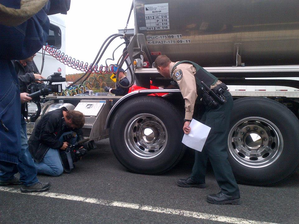 Contrôleur routier et caméras de télévision devant une remorque citerne.