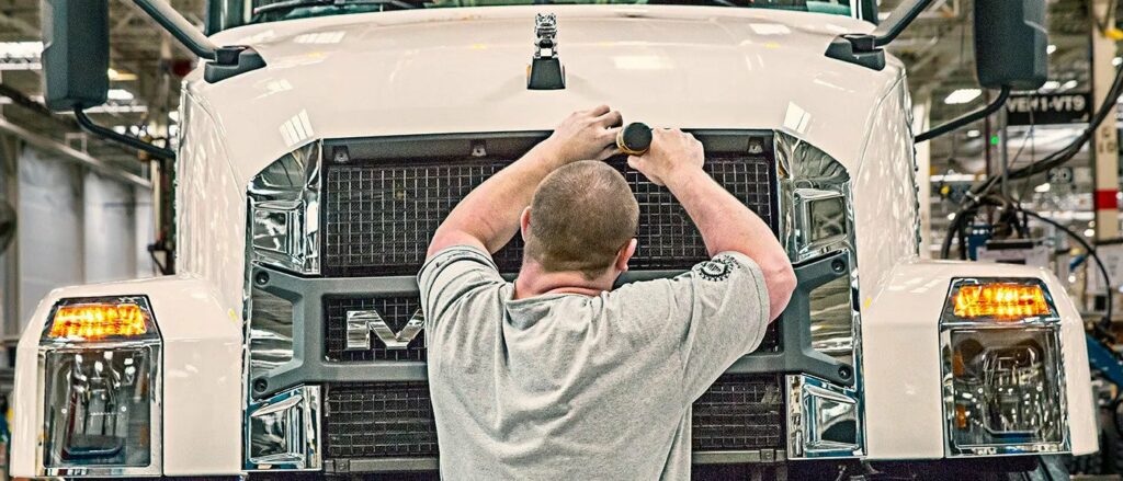 Ouvrier installe la calandre d’un camion Mack sur la chaîne de montage