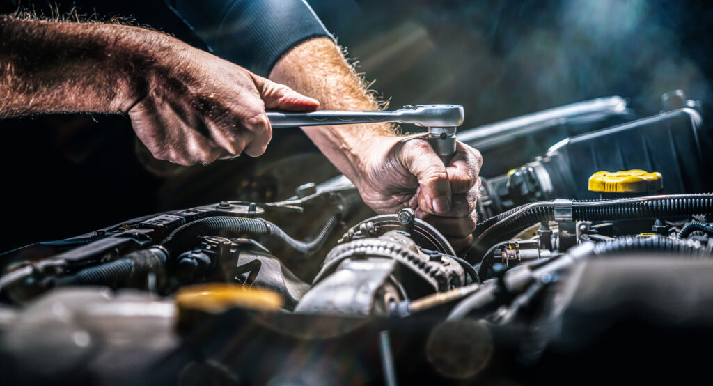Main de mécanicien qui manipule un outil dans un compartiment moteur