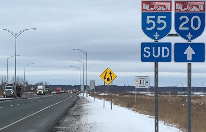 Camions qui circulent vus de face et panneaux des autoroutes 55 et 20