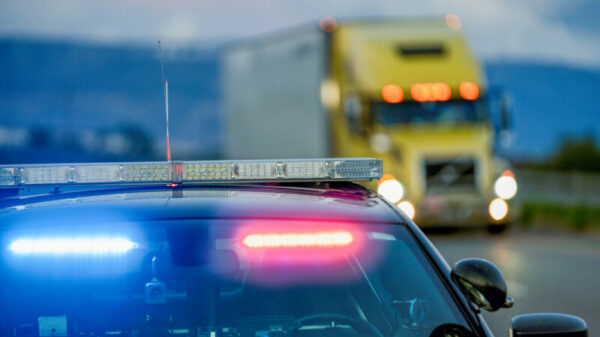 A Highway Patrol Car With The Lights On, Pulling A Driver Over For Speeding As A Semi Truck Drives Passed alternate text for this image
