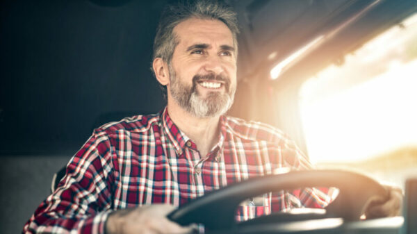 Happy mature truck driver driving his truck to a warehouse. alternate text for this image