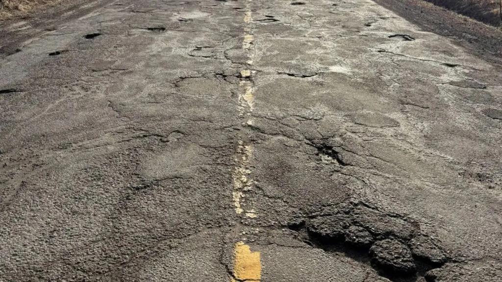 Gros plan de route asphaltée avec ornières et nids-de-poule.