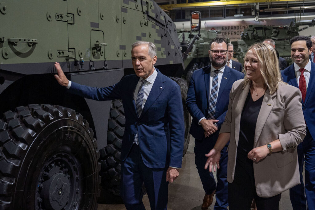 Mark Carney pose la main sur un véhicule militaire de General Dynamics, à London en Ontario.
