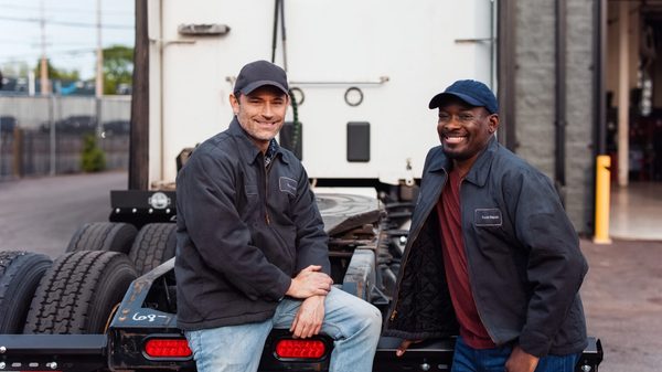 Two Mechanics Smiling Near Truck Trailer in Outdoor Industrial Setting alternate text for this image