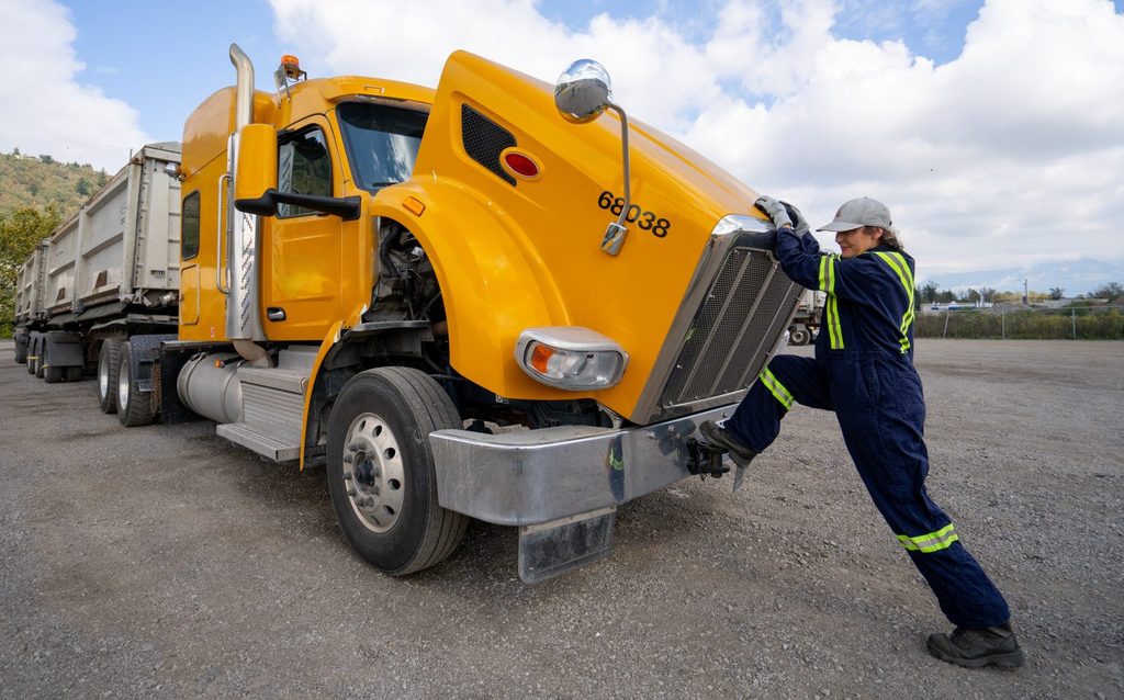 Femme chauffeuse ouvre le capot d’un tracteur Peterbilt jaune