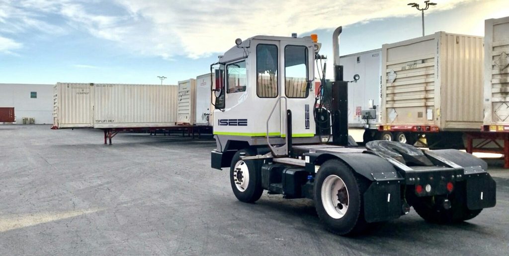 Tracteur de manœuvre autonome Isee vu de ¾ arrière avec remorques dans une cour en arrière-plan